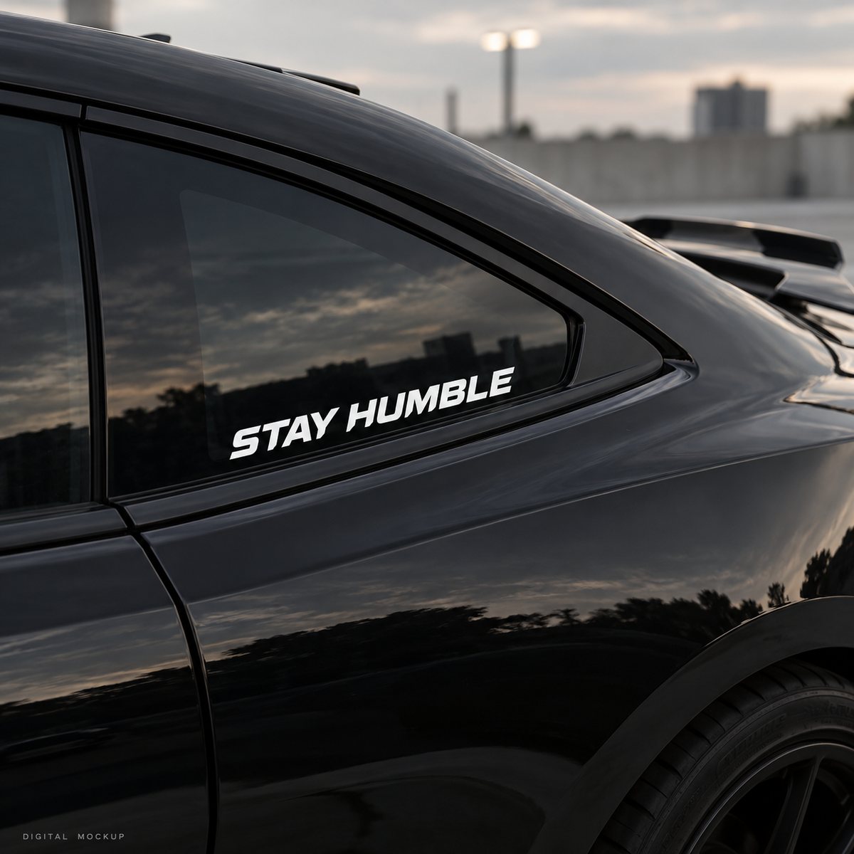 Digital mockup: white Stay Humble vinyl lettering on a black car window. Illustrative placement; not a photograph of an installed physical product.